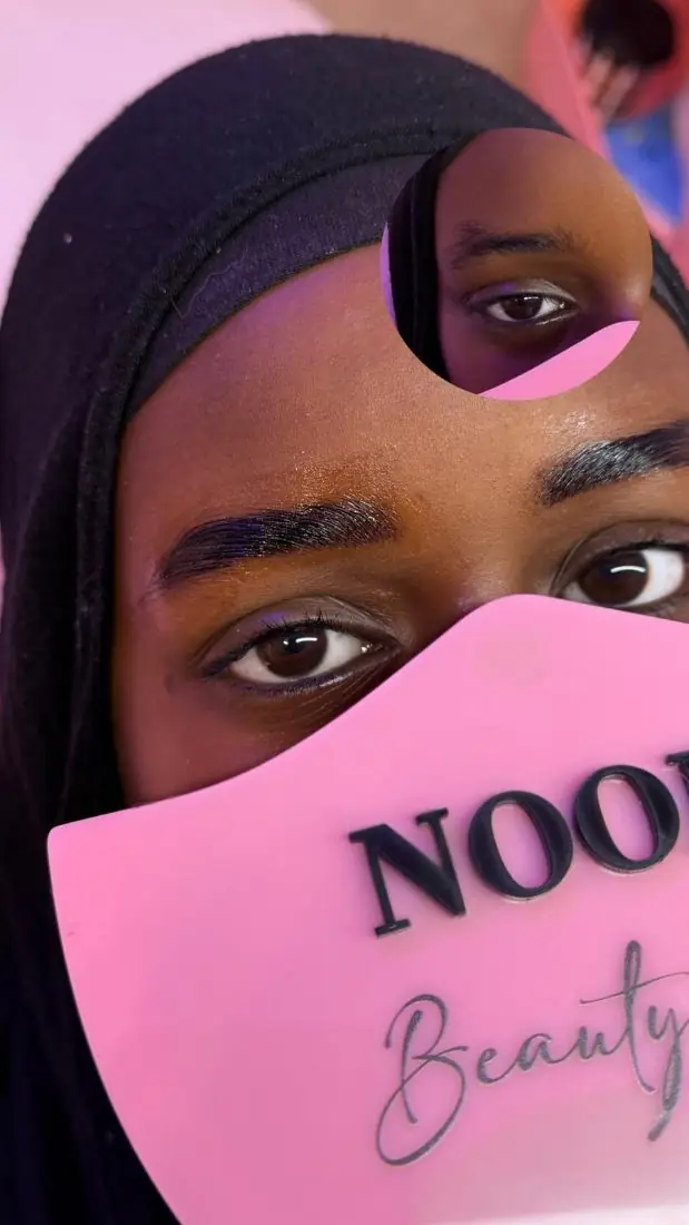 A client with lifted lashes and laminated brows holding a Noor mirror